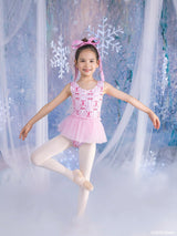 A young girl ballerina posing in a pink Barbie in The Nutcracker leotard with ballet shoe prints, a pink tutu, and white tights, set against a magical winter forest backdrop with snowflakes and sheer white drapes.